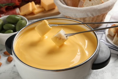 Photo of Pot of tasty cheese fondue and forks with bread pieces on white table, closeup