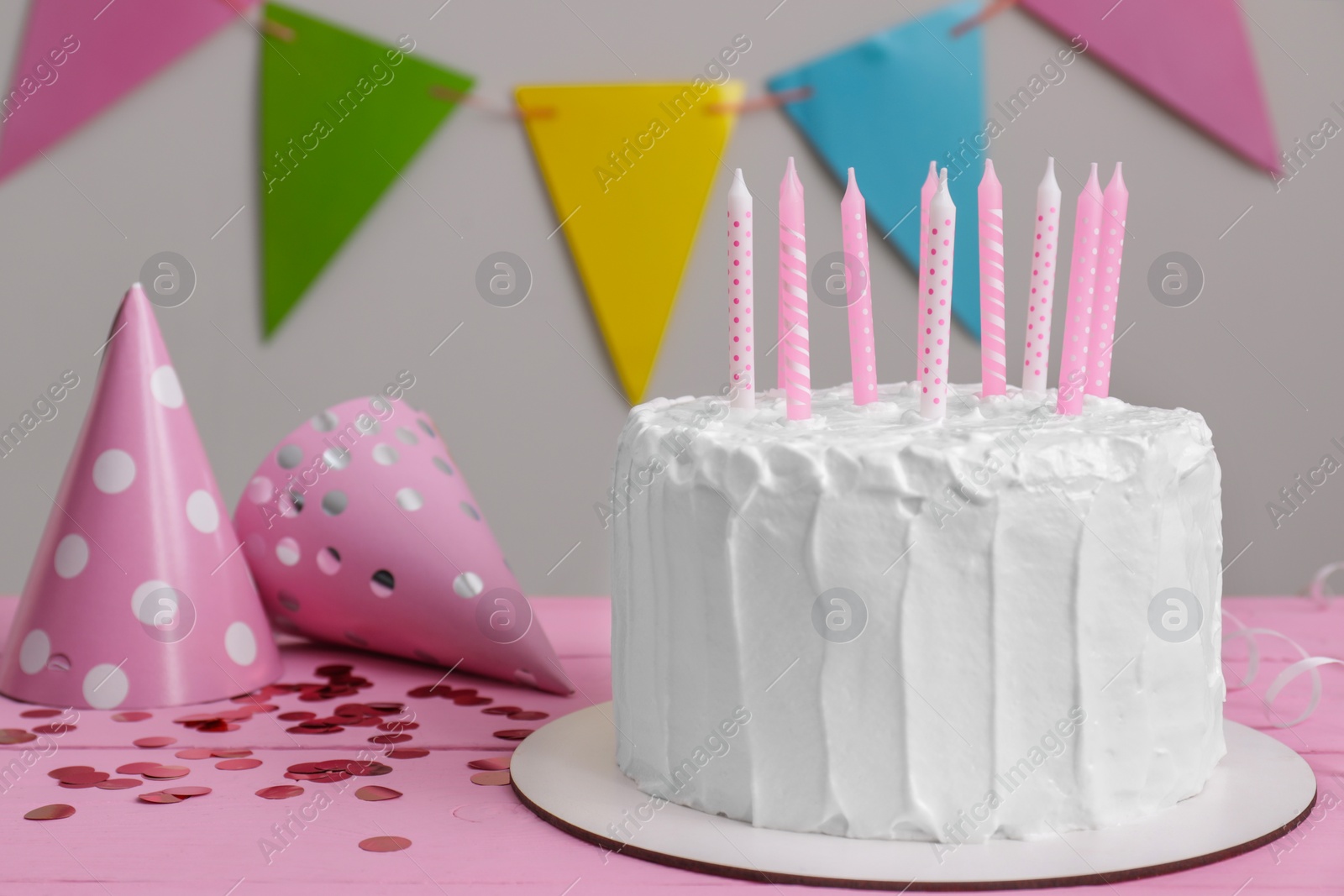 Photo of Delicious cake with candles and party hats on pink wooden table. Space for text