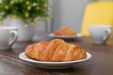 Plate with tasty freshly baked croissant on table