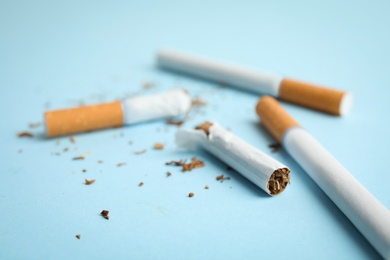 Photo of Broken and whole cigarettes on light blue background, closeup. Quitting smoking concept