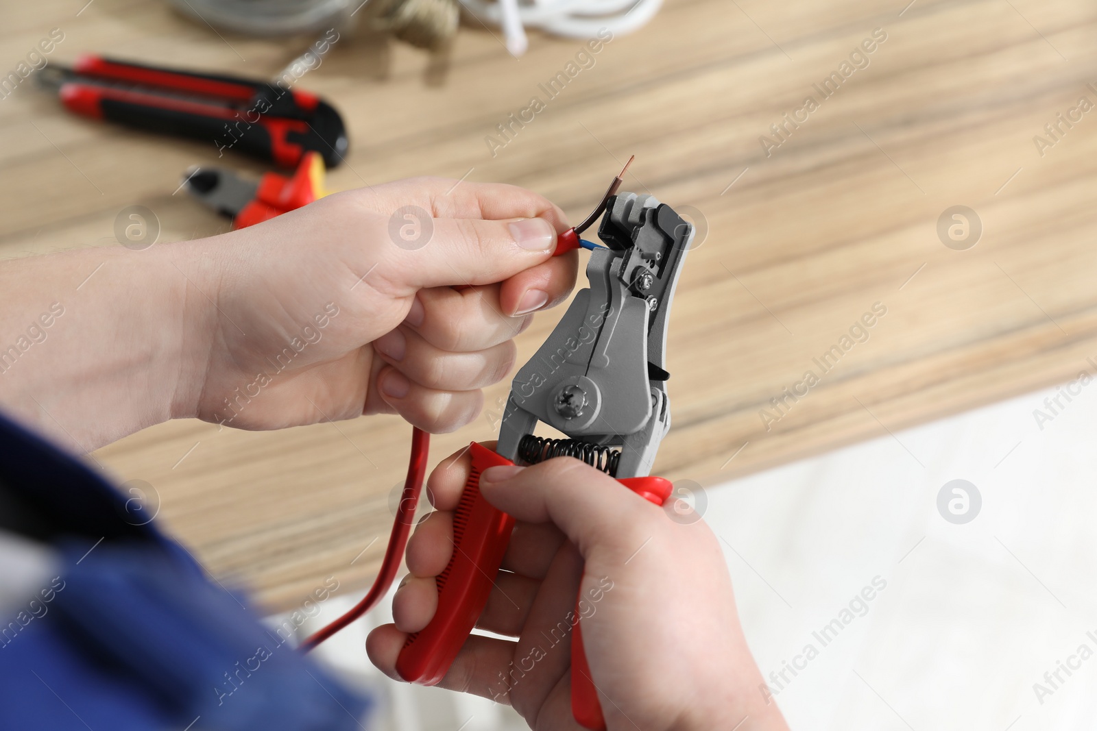 Photo of Professional electrician stripping wiring at wooden table, above view