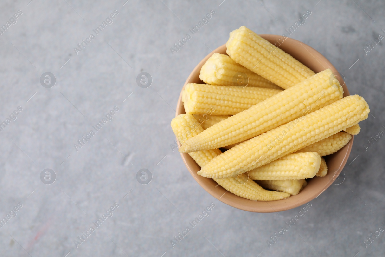 Photo of Tasty fresh yellow baby corns in bowl on grey table, top view. Space for text