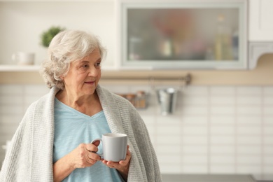 Elderly woman with cup of tea in kitchen. Space for text