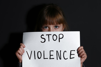 Photo of Abused little girl with sign STOP VIOLENCE near black wall