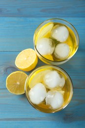 Delicious cocktails with lemon and ice balls on light blue wooden table, flat lay