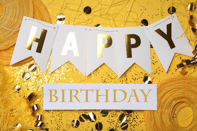 Flat lay composition with greeting HAPPY BIRTHDAY  and party decor on yellow background