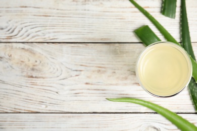 Photo of Fresh aloe drink in glass and leaves on white wooden table, flat lay. Space for text