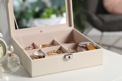Jewelry box with many different accessories and perfume on white wooden table indoors, closeup