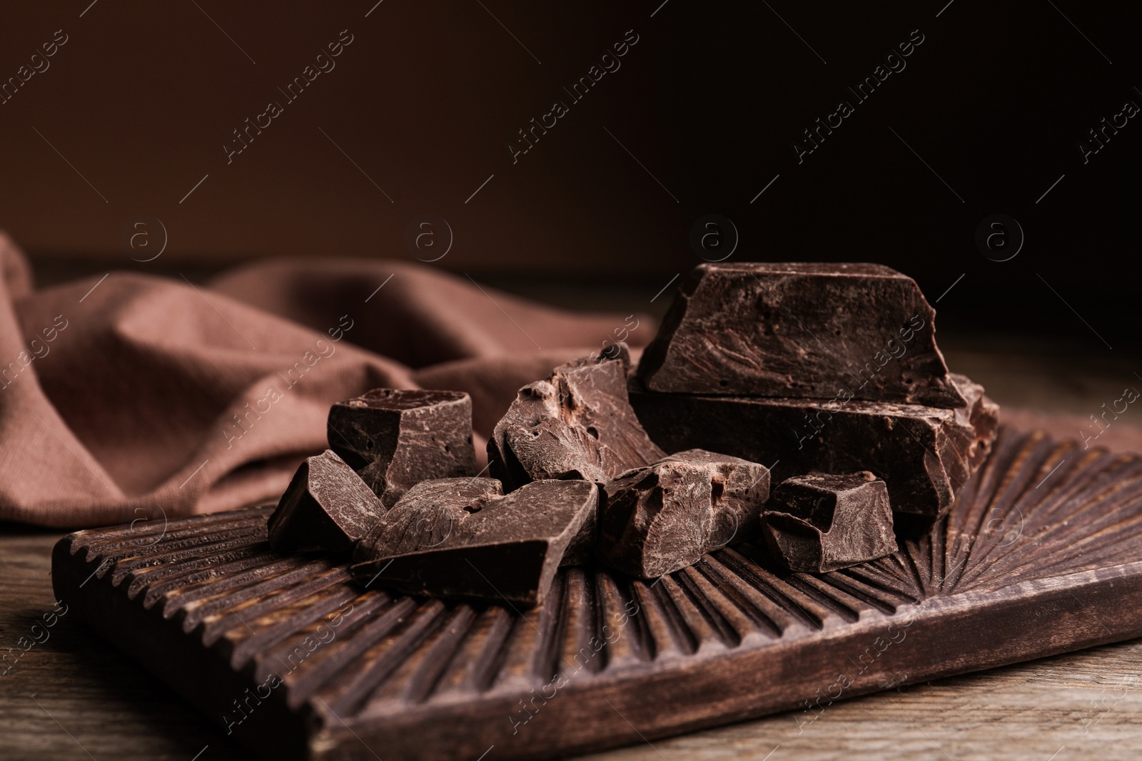 Photo of Pieces of tasty dark chocolate on wooden board