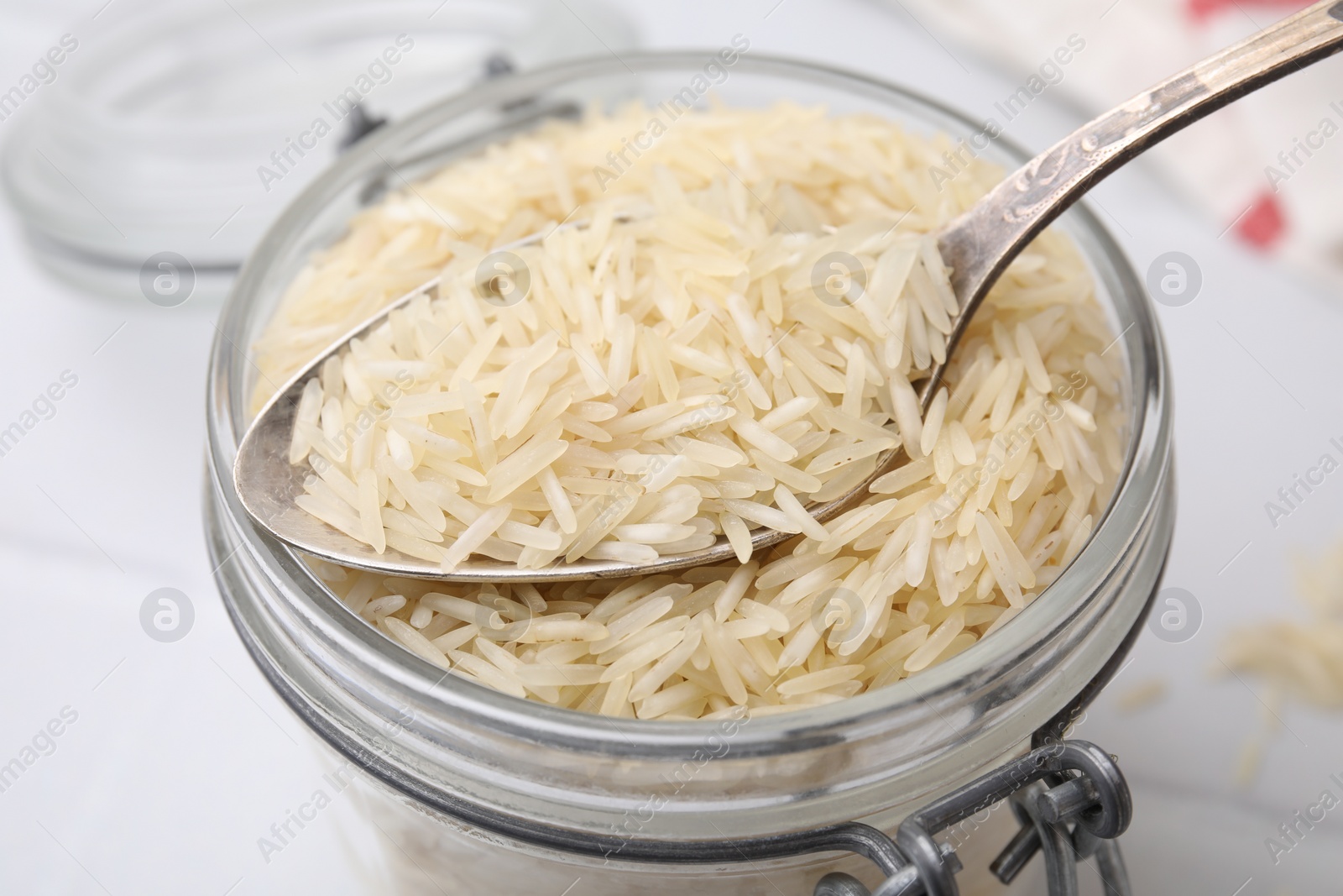 Photo of Glass jar and spoon with raw rice on table, closeup