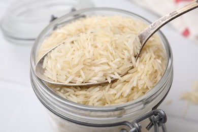 Photo of Glass jar and spoon with raw rice on table, closeup