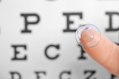 Woman holding contact lens near eye chart, closeup