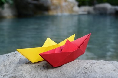 Photo of Beautiful yellow and red paper boats on stone near pond, closeup