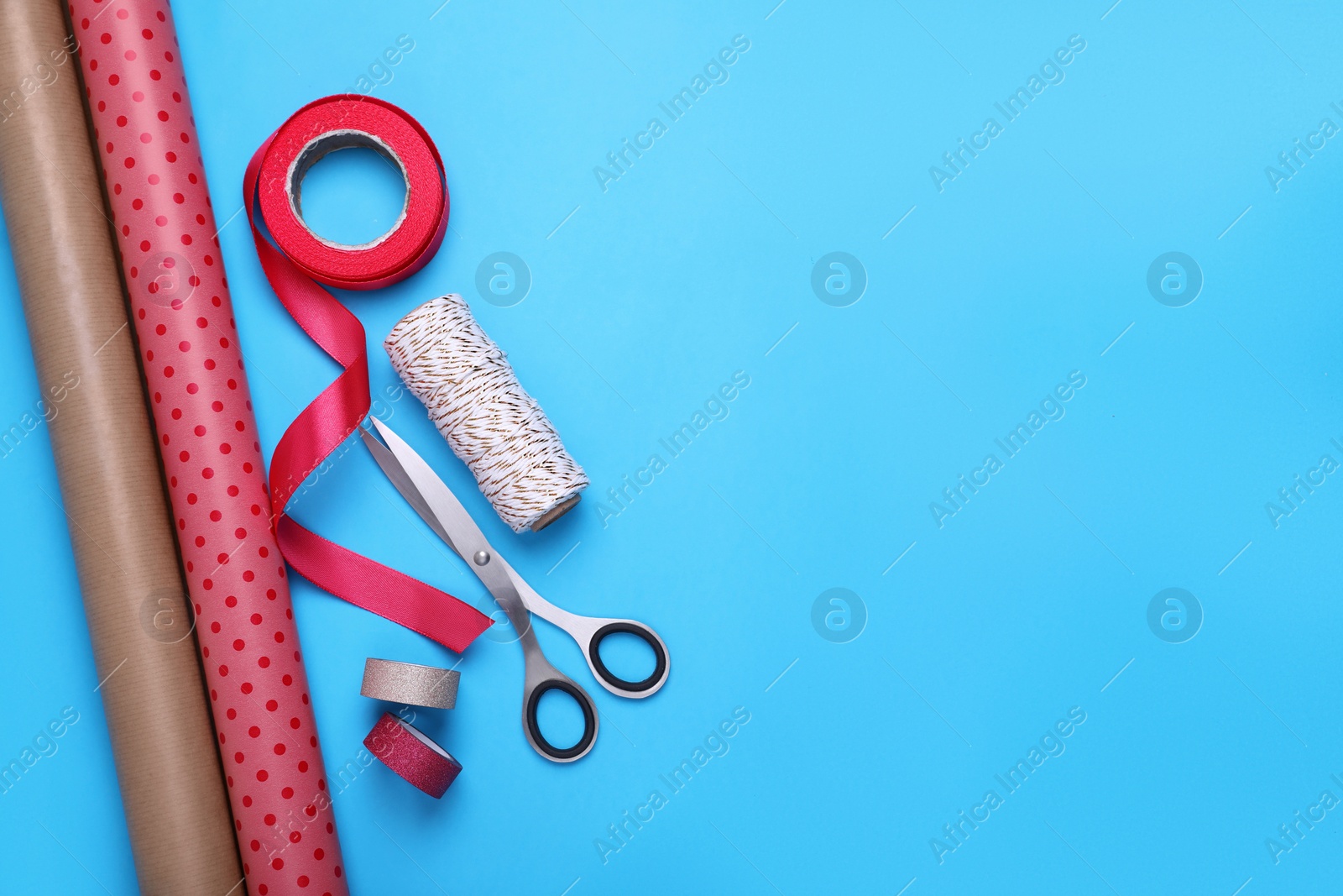 Photo of Rolls of wrapping papers, scissors and ribbons on light blue background, flat lay. Space for text