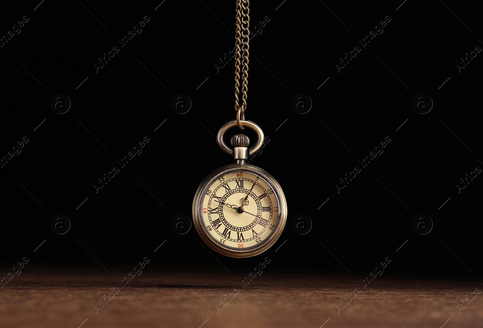 Photo of Stylish pendulum above wooden table on black background. Hypnotherapy session