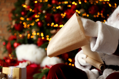 Santa Claus reading wish list against blurred festive lights, closeup