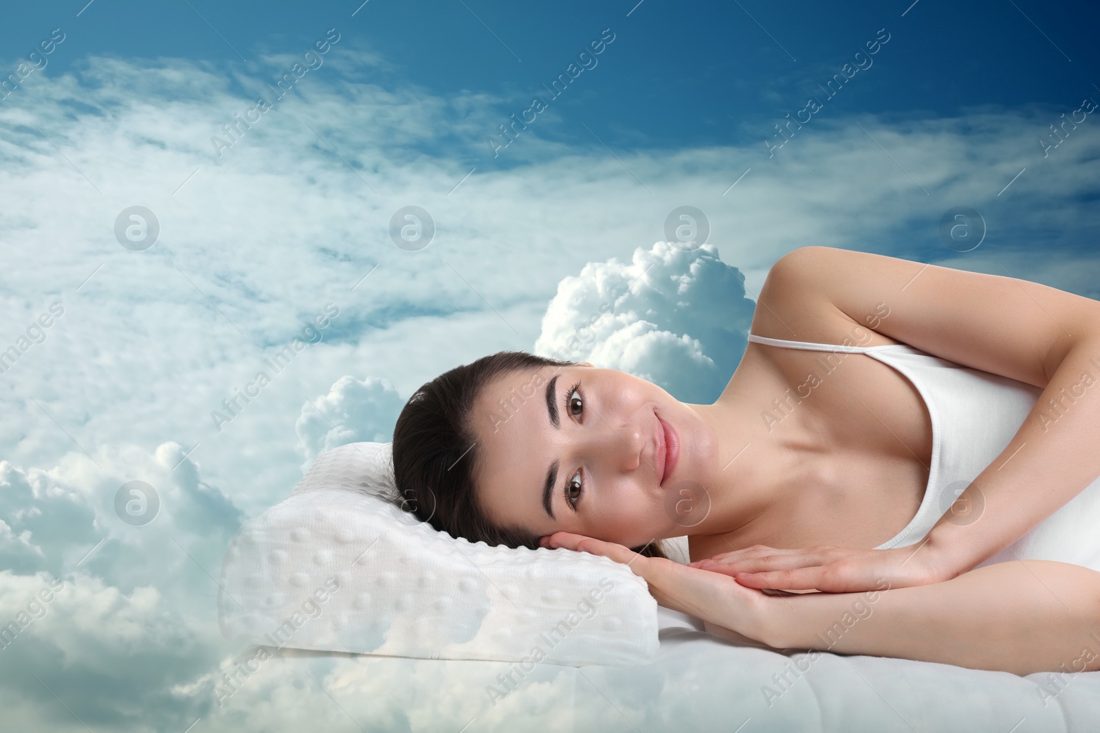 Image of Woman lying on orthopedic pillow against blue sky