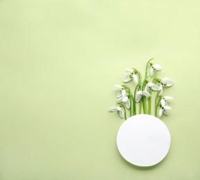 Beautiful snowdrops and paper card on light background, flat lay. Space for text