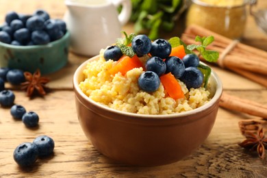 Photo of Tasty millet porridge with blueberries, pumpkin and mint in bowl on wooden table, closeup