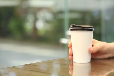 Photo of Woman holding takeaway paper cup at table, closeup and space for text. Coffee to go