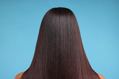 Woman with healthy hair after treatment on light blue background, back view