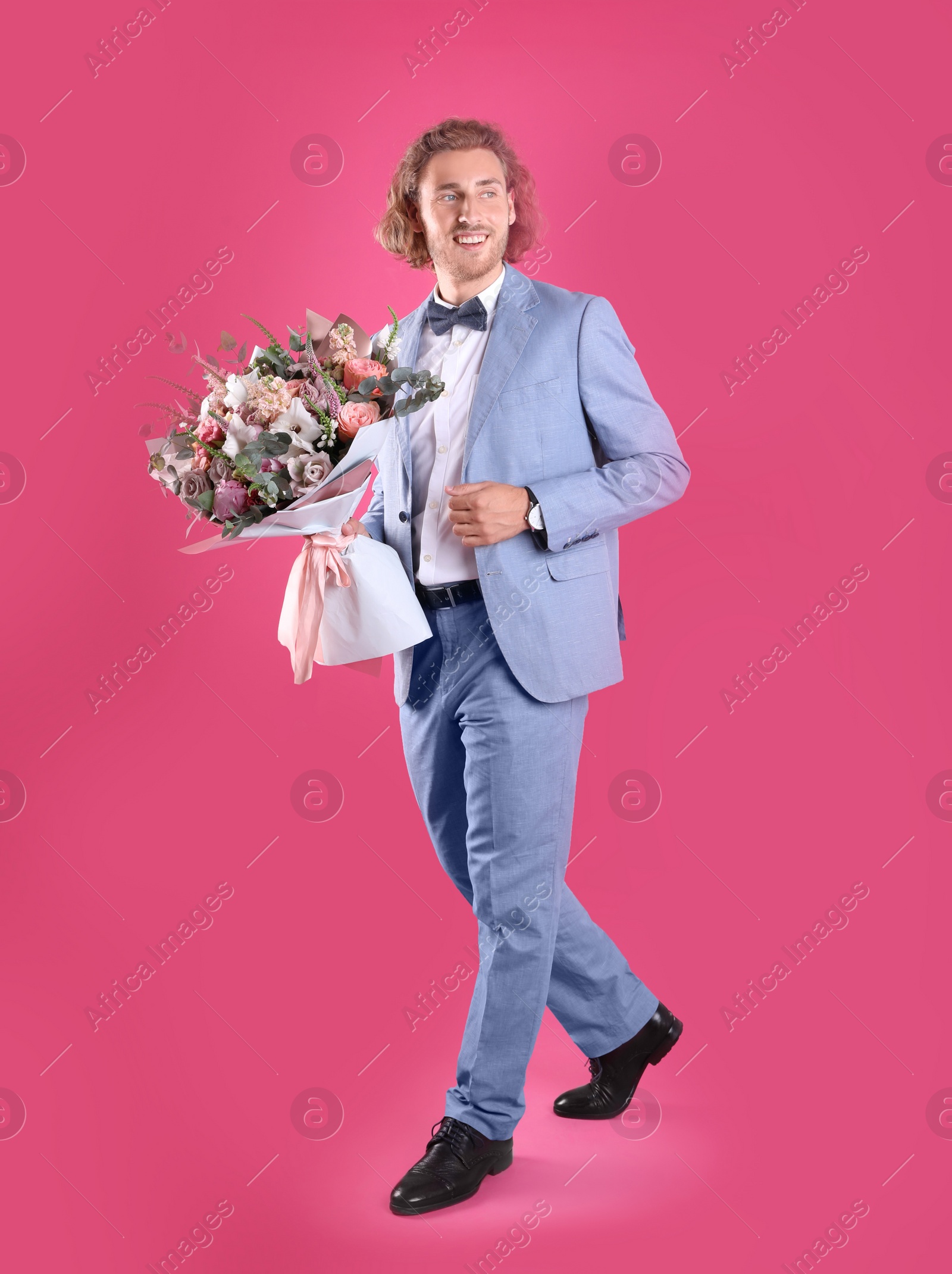 Photo of Young handsome man in stylish suit with beautiful flower bouquet on pink background