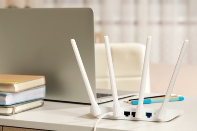 Photo of New Wi-Fi router near laptop on white table indoors