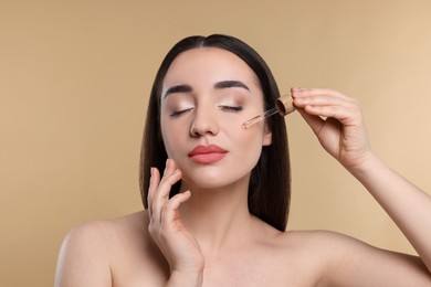 Young woman applying essential oil onto face on beige background