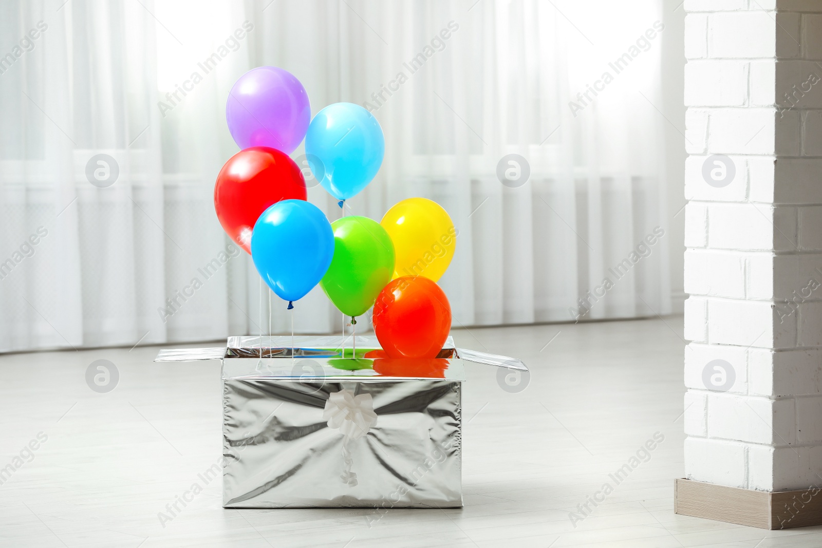 Photo of Gift box with bright air balloons on floor indoors. Space for text