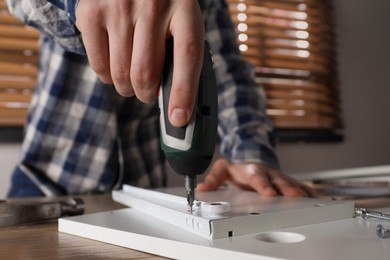 Man assembling furniture at table indoors, closeup