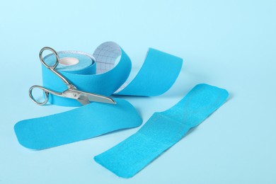 Photo of Scissors, bright kinesio tape roll and pieces on light blue background