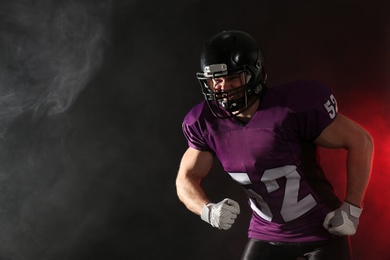 Photo of American football player wearing uniform on dark background. Space for text