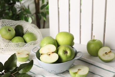 Fresh green apples with water drops and leaves on white table