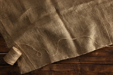 Photo of Burlap fabric and spool of thread on wooden table, top view