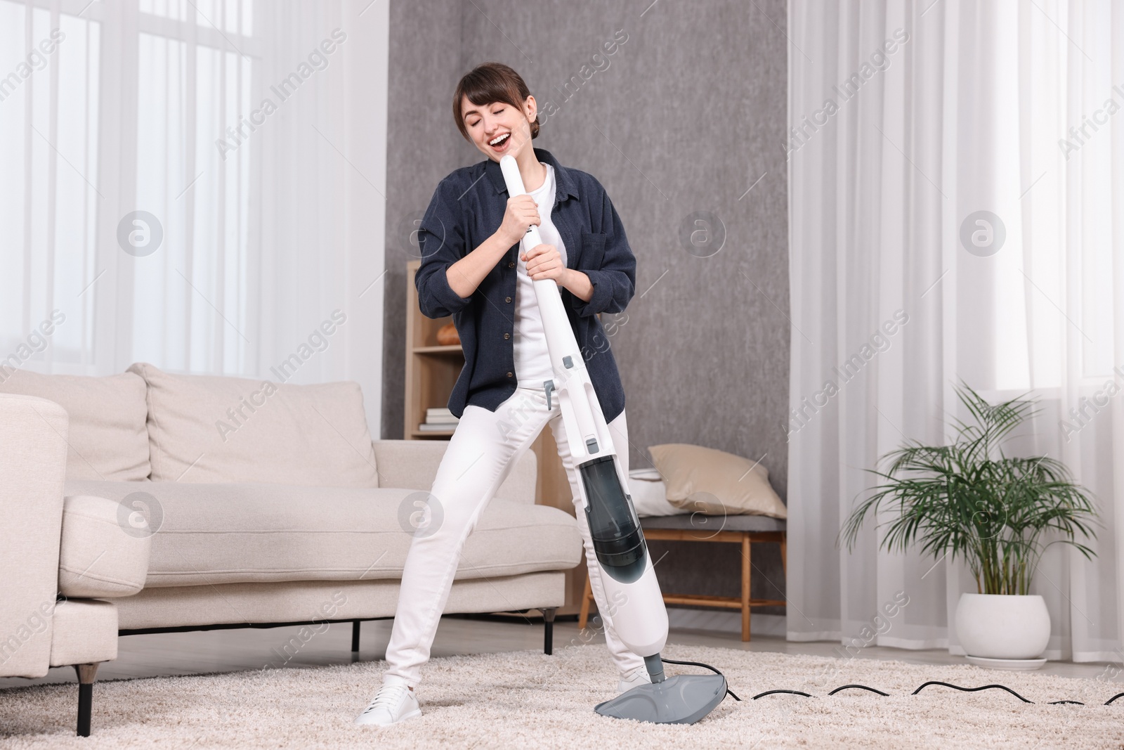 Photo of Happy young housewife having fun while cleaning carpet at home