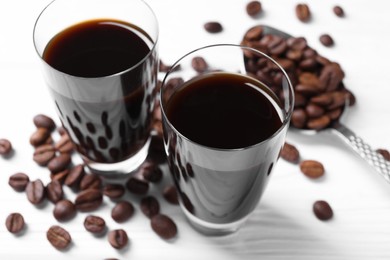 Shot glasses of coffee liqueur and beans on white table, closeup