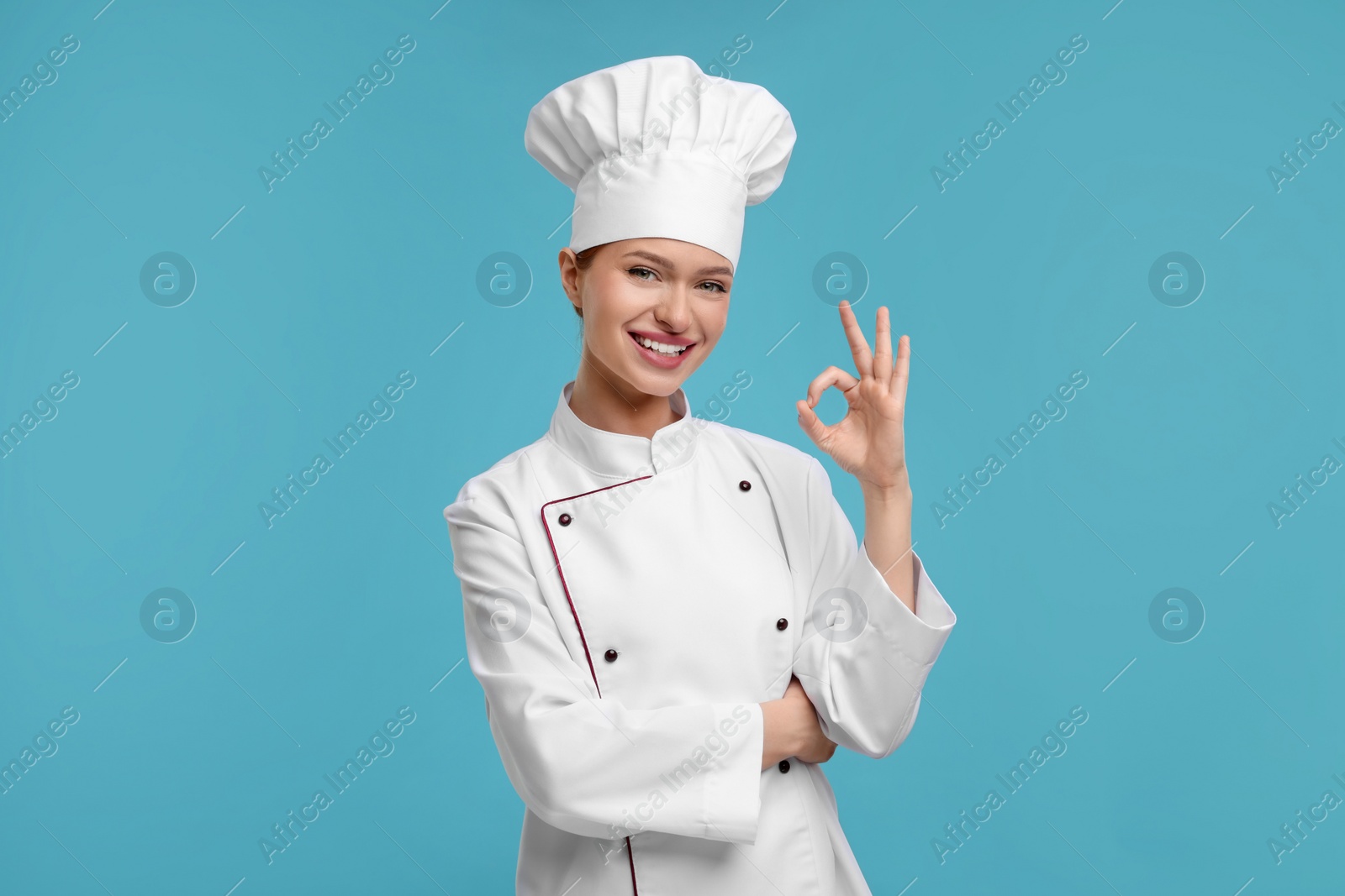 Photo of Happy woman chef in uniform showing OK gesture on light blue background