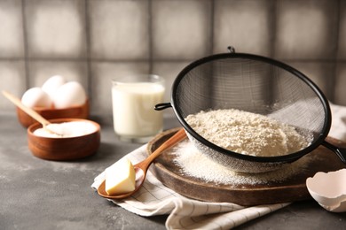 Making dough. Flour in sieve, spoon and butter on grey textured table, closeup