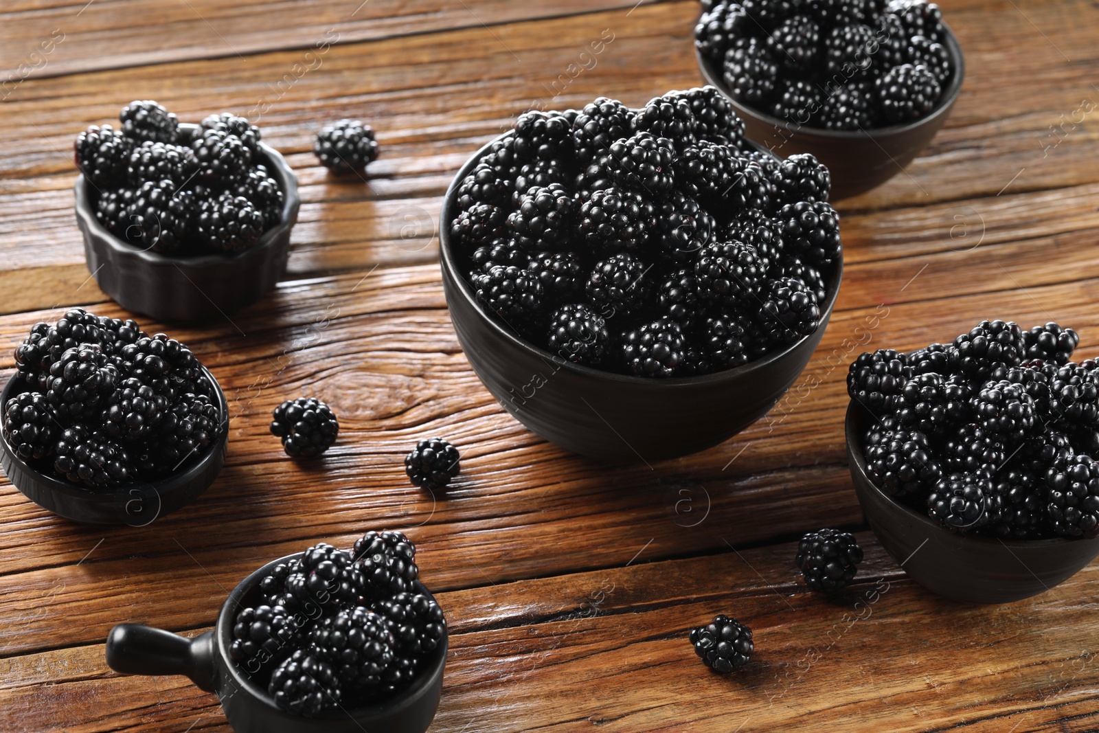 Photo of Ripe blackberries in bowls on wooden table