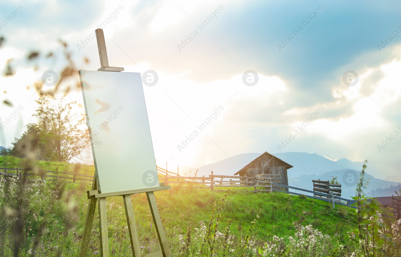 Image of Wooden easel with blank canvas and picturesque view of village on mountain slopes