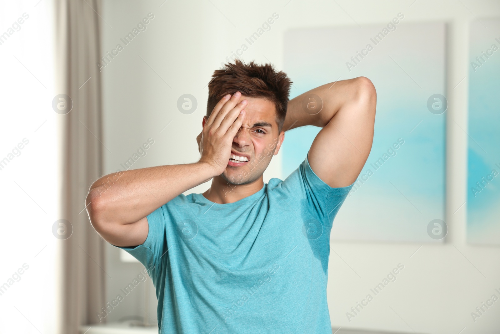 Photo of Young man with sweat stain on his clothes indoors. Using deodorant