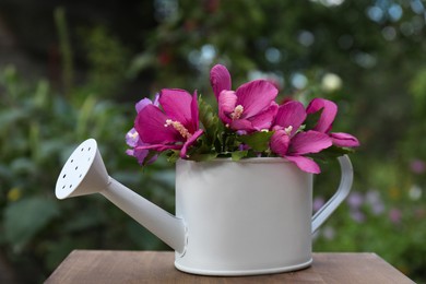 Photo of Beautiful flowers in watering can on wooden table outdoors
