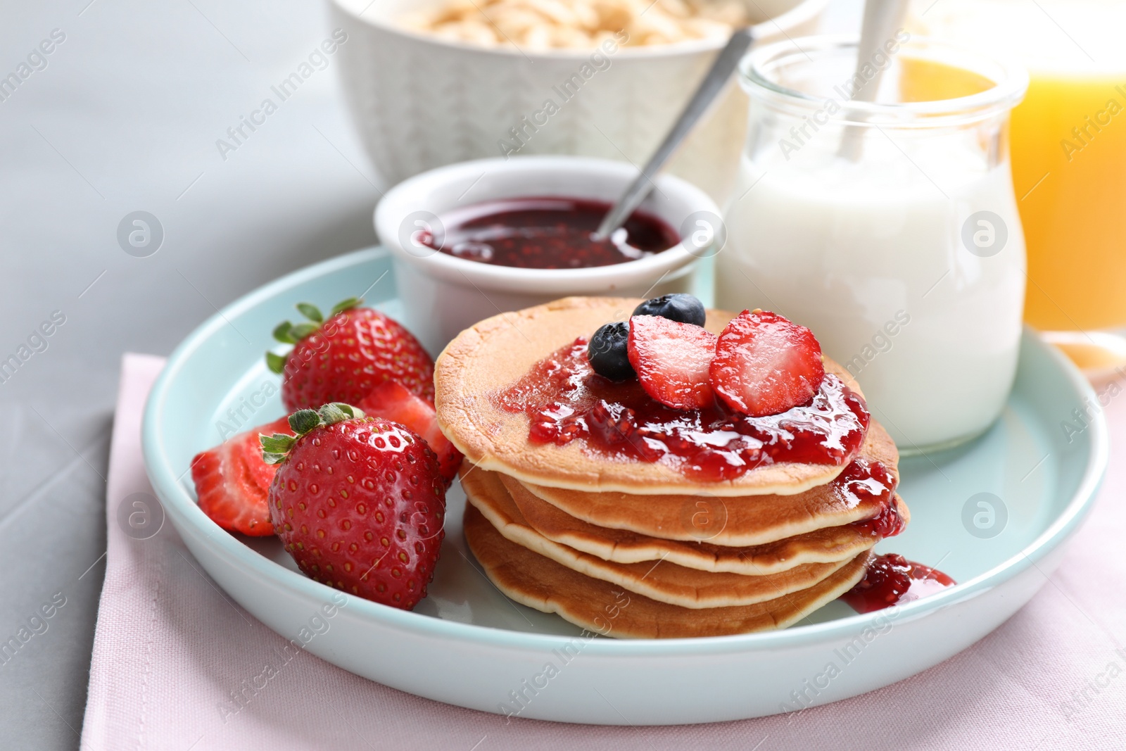 Photo of Fresh pancakes with jam and strawberries on light grey table. Healthy breakfast