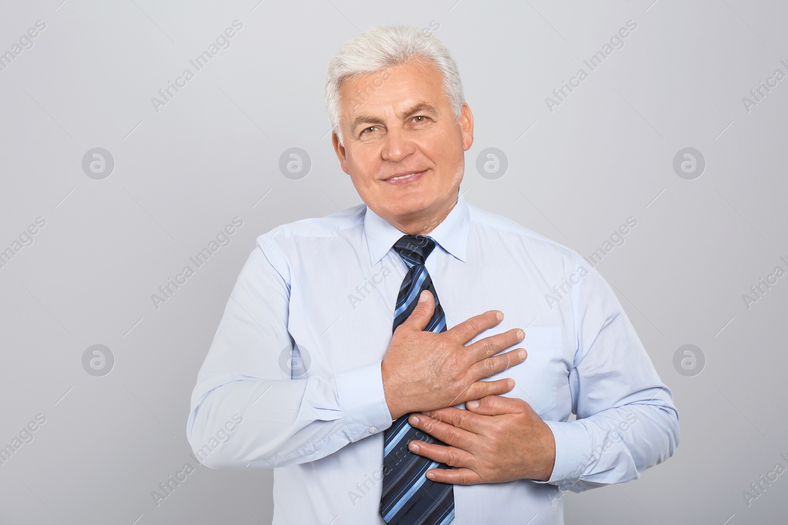 Photo of Grateful senior man with hands on chest against light grey background