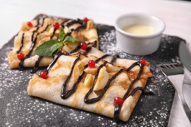 Photo of Thin pancakes served with sauce and berries on slate plate, closeup