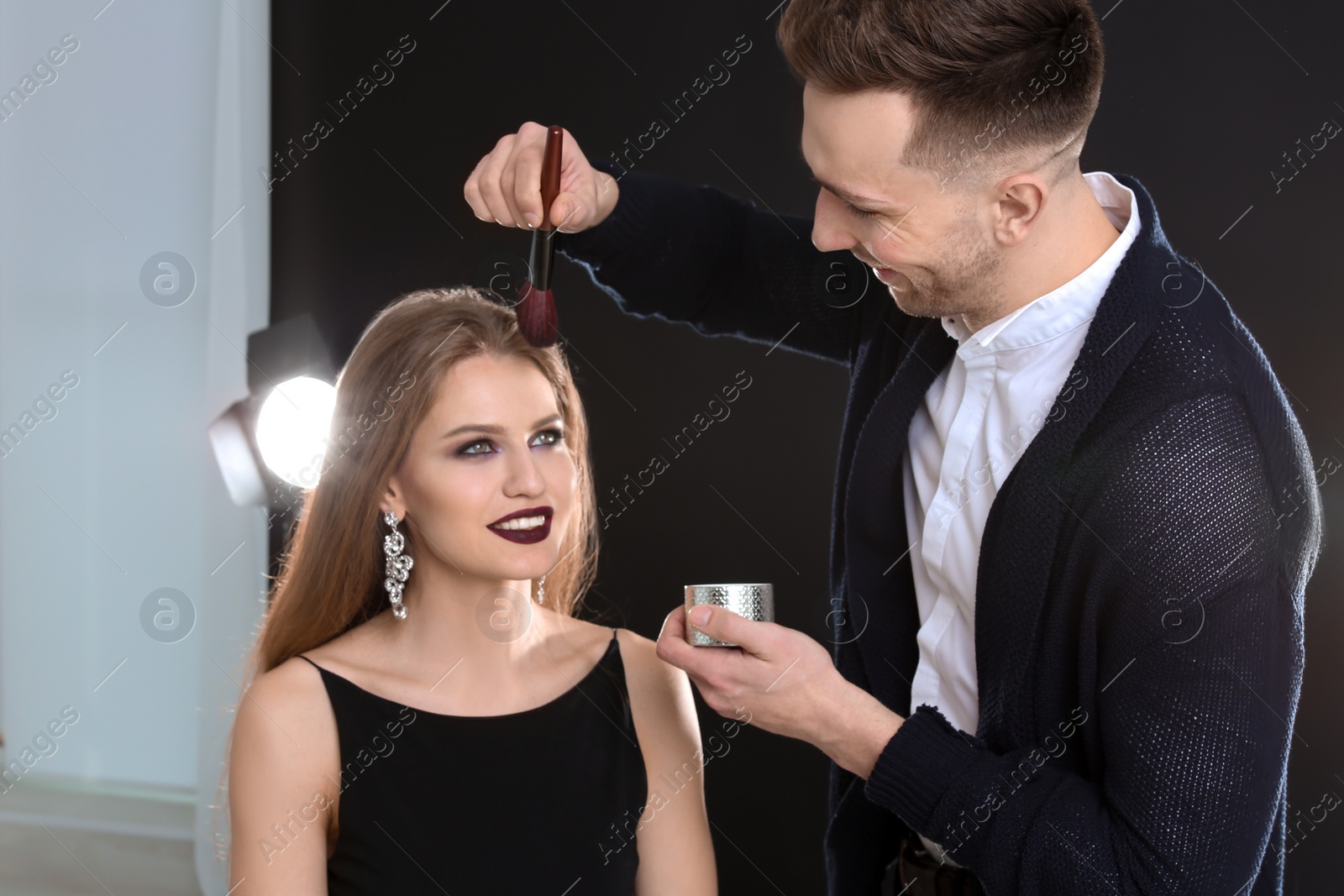 Photo of Professional makeup artist working with beautiful young woman in photo studio