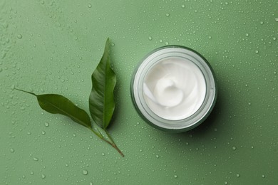 Photo of Glass jar of face cream and leaves on wet green surface, flat lay