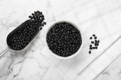 Photo of Bowl and scoop of raw black beans on white marble table, flat lay