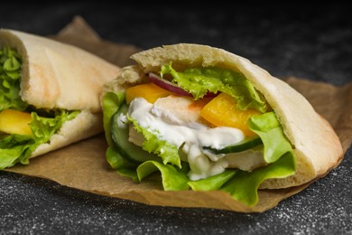 Delicious pita sandwiches with chicken breast and vegetables on black table