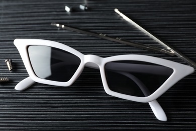 Photo of Stylish female sunglasses and fixing tools on black wooden table
